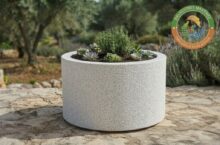 Jardinera cilindrica rugosa de granito en piedra artificial color blanco y marfil para decoracion exterior.